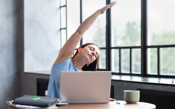 Woman stretching neck and arms while sitting at a desk